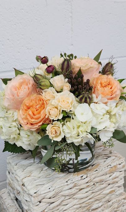 Low arrangement of peach and cream roses with white hydrangeas in a clear glass vase.