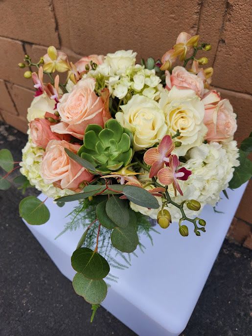 Low arrangement of peach and cream roses, white hydrangea, orchids and a green succulent in a compact design