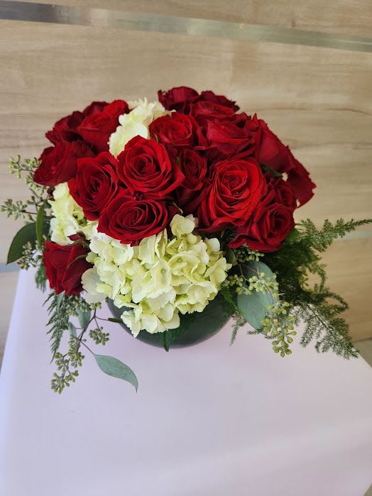 Low round arrangement of red roses and white hydrangeas in a green glass vase
