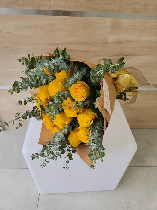 Wrapped bouquet of bright yellow roses and eucalyptus laid on a white stand