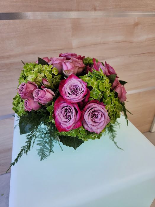 Low round arrangement of pink and lavender roses with green hydrangeas in a compact mound.