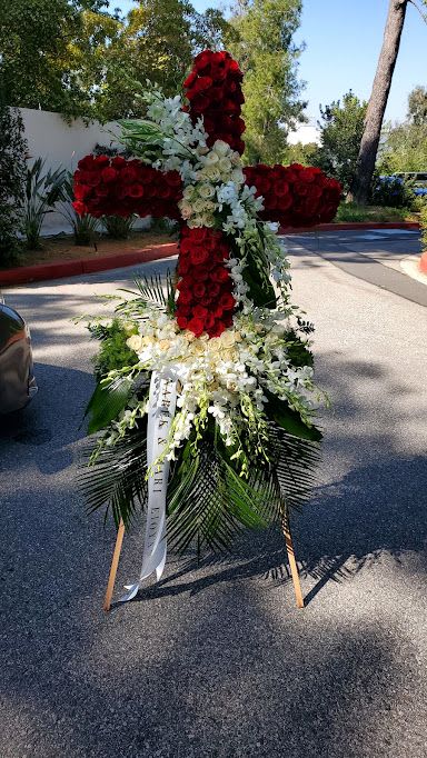 Tall standing cross of red and white flowers on an easel with cascading white blooms