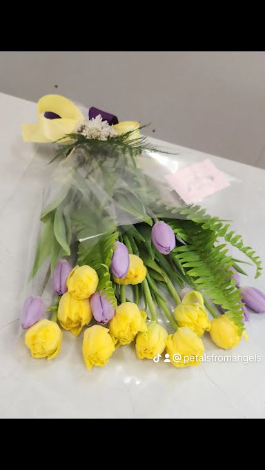 Wrapped bouquet of yellow and lavender tulips with fern fronds and a yellow ribbon