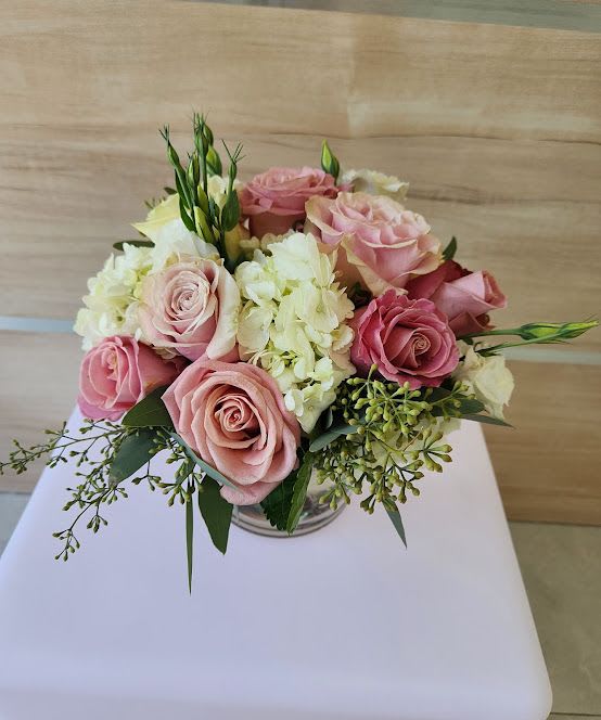 Low arrangement of pink roses and white hydrangeas in a clear glass vase