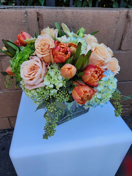 Low arrangement of peach roses and orange tulips with green hydrangeas in a clear glass vase