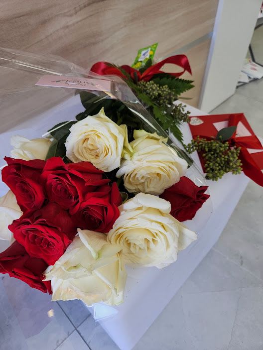 Bouquet of red and white roses with a red ribboned gift box on a white surface
