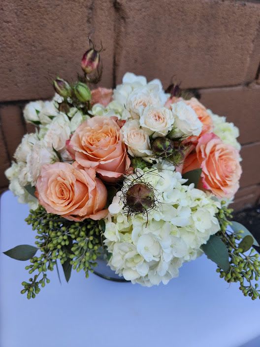 Low arrangement of peach roses, cream spray roses, and white hydrangeas in a round vase