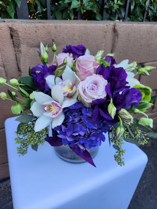 Low glass vase of purple and blue hydrangea, white orchids, and light pink roses in a compact arrangement