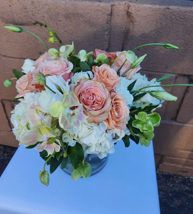Low arrangement of peach roses, white hydrangeas, and green orchids in a clear glass vase