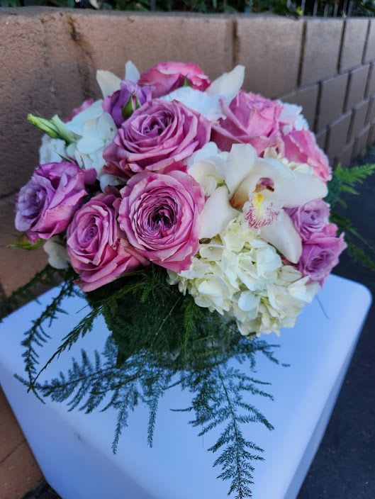 Round arrangement of pink roses, white hydrangeas, and orchids on a white pedestal