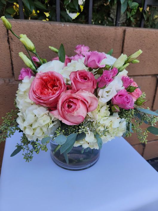 Round arrangement of pink roses, white hydrangeas, and lisianthus in a clear glass vase