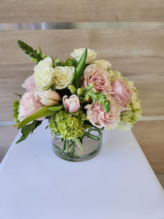 Low arrangement of pale pink roses, white roses, tulips, and green hydrangea in a clear glass vase