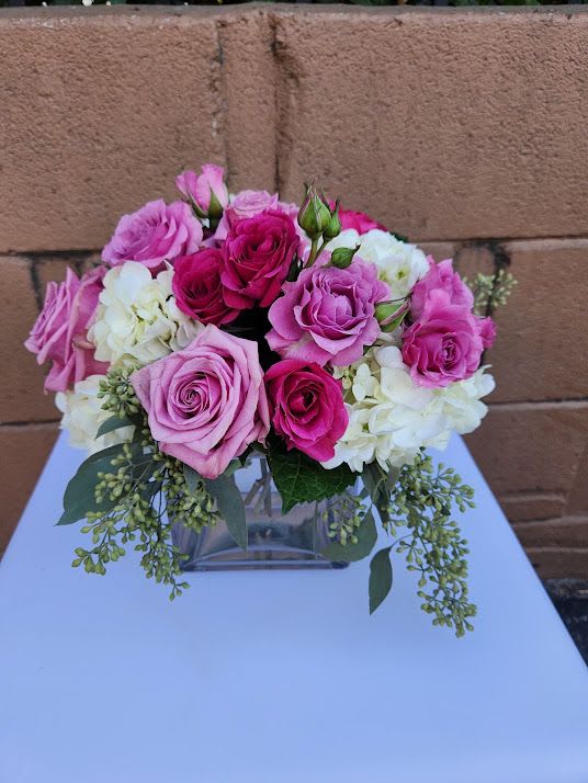 Low arrangement of pink roses and white hydrangeas in a clear glass cube vase