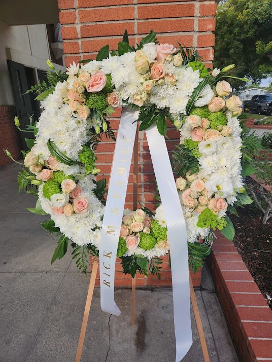 Standing wreath of white mums and peach roses with ribbon on wooden easel