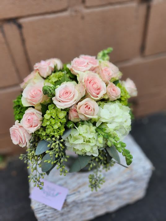 Round arrangement of pale pink roses with white and green hydrangeas in a clear glass vase