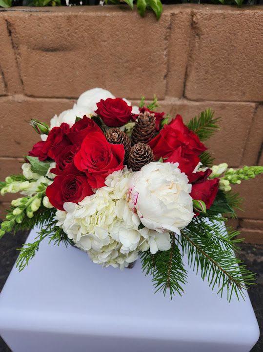 Low arrangement of red roses, white hydrangeas, and pinecones with evergreen in a vase