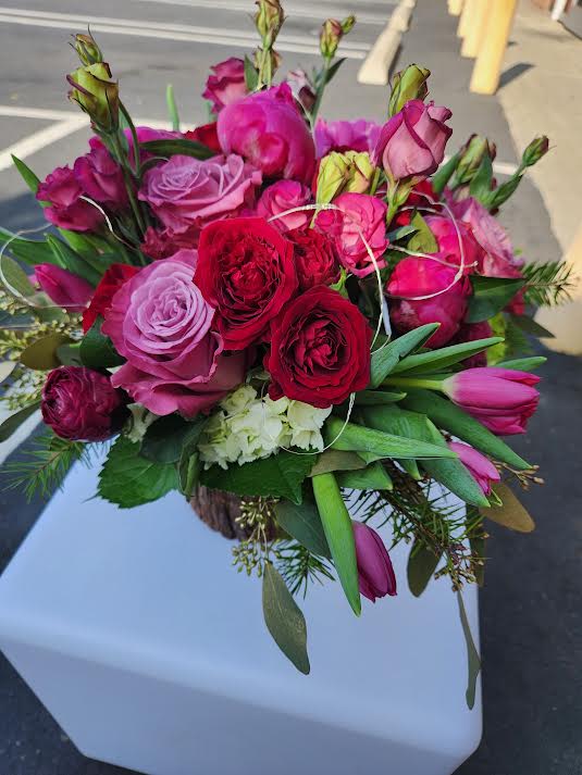 Round arrangement of red and pink roses and tulips in a rustic container