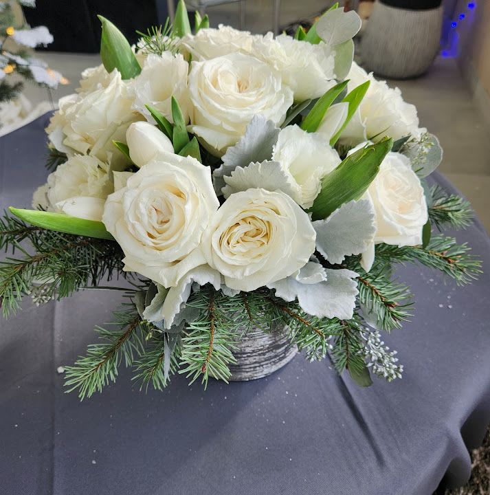 Low arrangement of white roses and tulips with pine branches in a gray pot