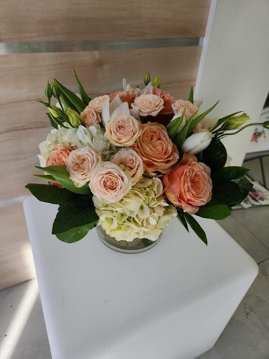 Low arrangement of peach roses and white hydrangeas in a clear glass vase on a white pedestal