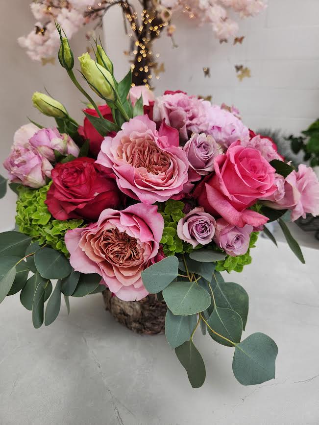 Low arrangement of pink and red roses with green hydrangea in a rustic container