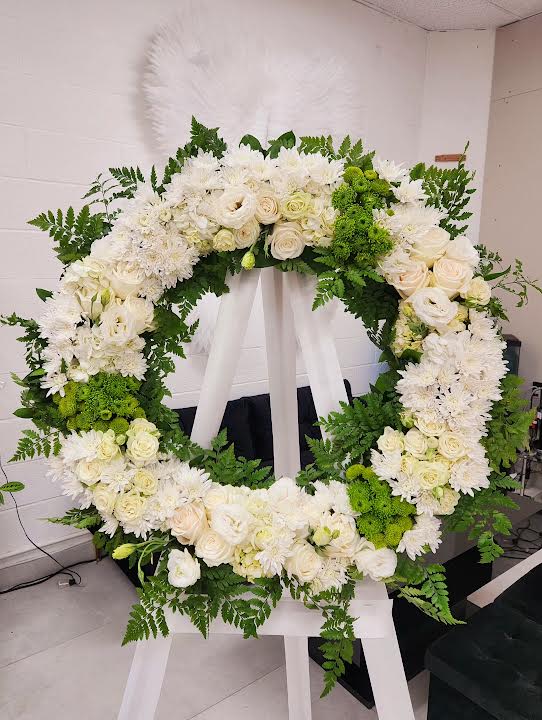Large white and green standing wreath of roses and mums on a white easel.