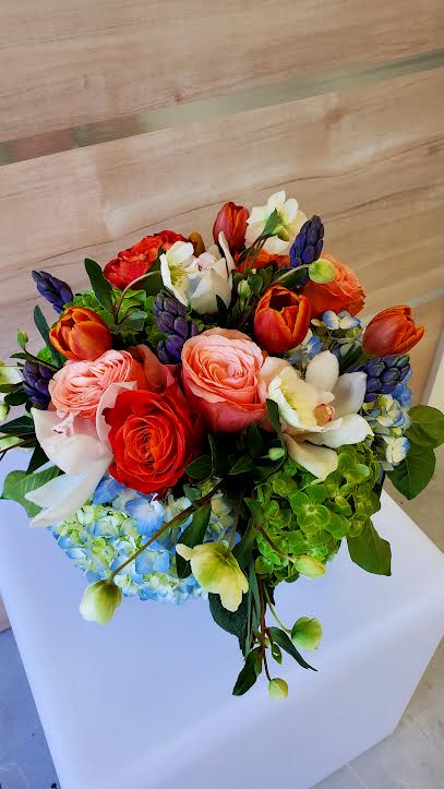 Compact arrangement of orange tulips, mixed roses, orchids, and blue and green hydrangeas.