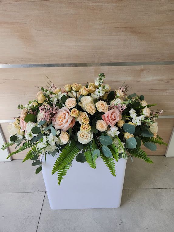 Low arrangement of peach and cream roses with white blooms and ferns in a white rectangular container