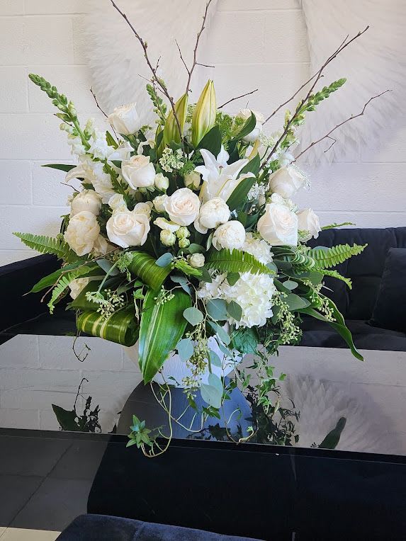 Large white and green floral arrangement with roses, lilies, and snapdragons in a white vase