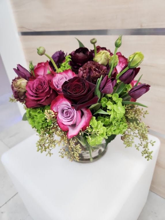 Compact bouquet of pink and burgundy roses with purple tulips and green hydrangeas in a glass vase