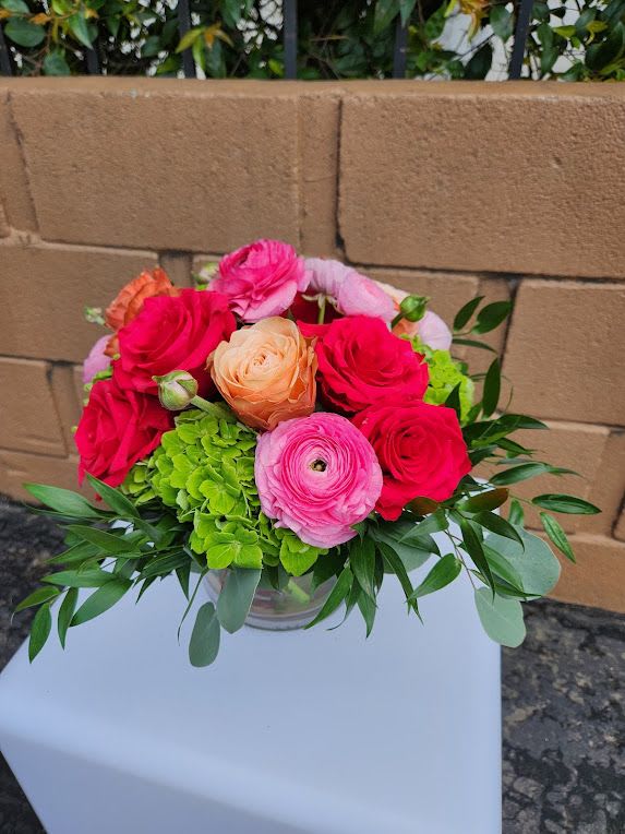 Short glass vase of pink roses, ranunculus, and green hydrangeas.