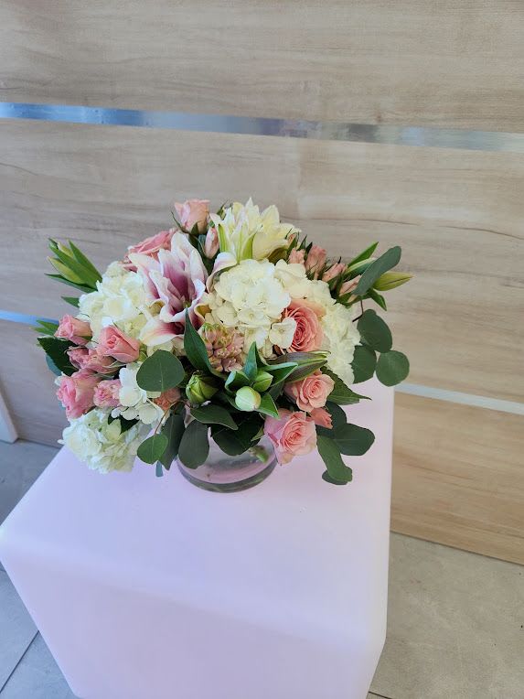 Low arrangement of pink roses, white hydrangeas, and lilies in a clear glass bowl vase