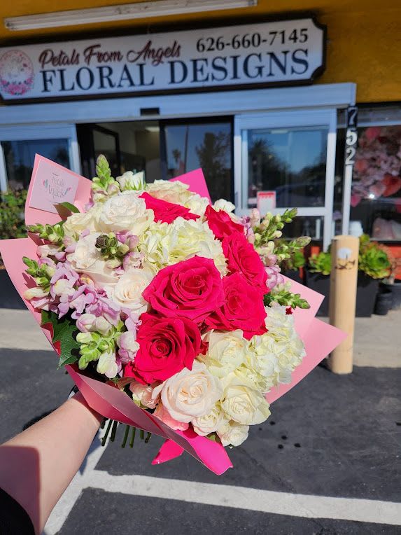 Hand-tied bouquet of hot pink and white roses with white hydrangeas and pastel blooms in pink wrap.