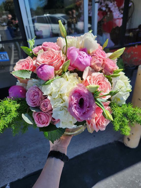 Low round arrangement of pink roses, lisianthus, and white hydrangeas in a clear glass bowl.