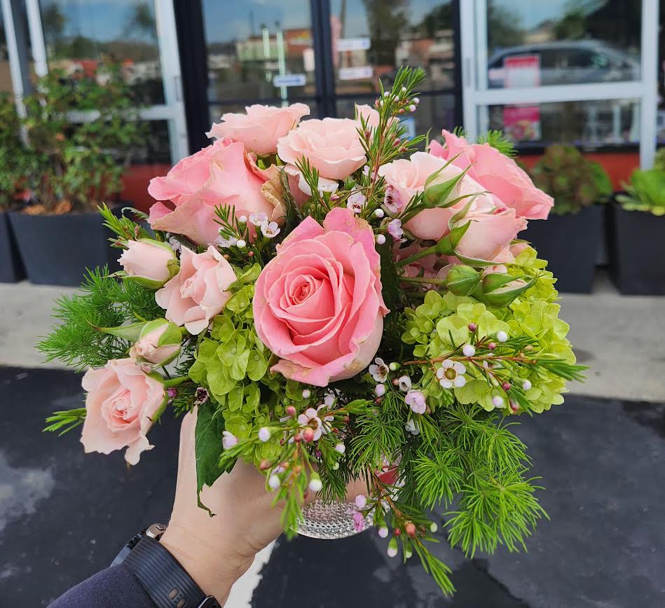Small bouquet of pink roses with green hydrangea in a clear glass vase held outdoors.