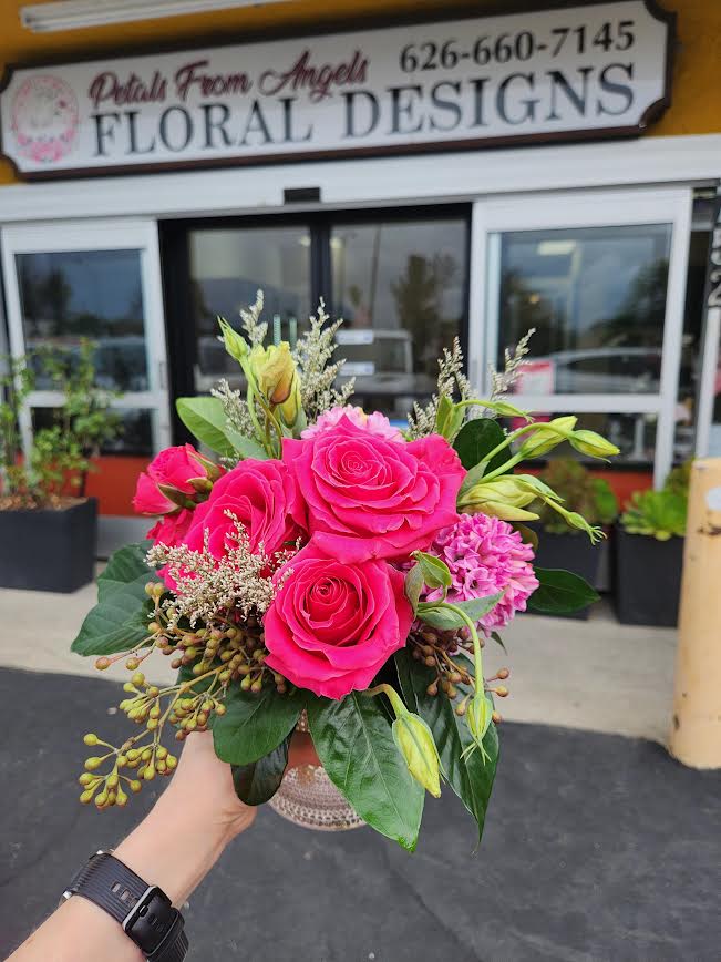 Compact arrangement of bright pink roses and mixed blooms in a small decorative vase, held outside a flower shop.