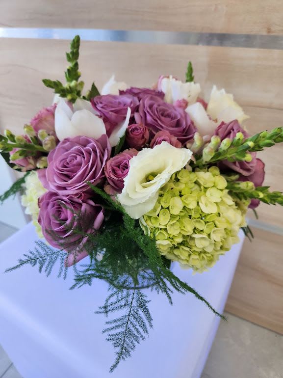 Low arrangement of lavender roses, white blooms, green hydrangea and trailing fern in a compact bouquet.