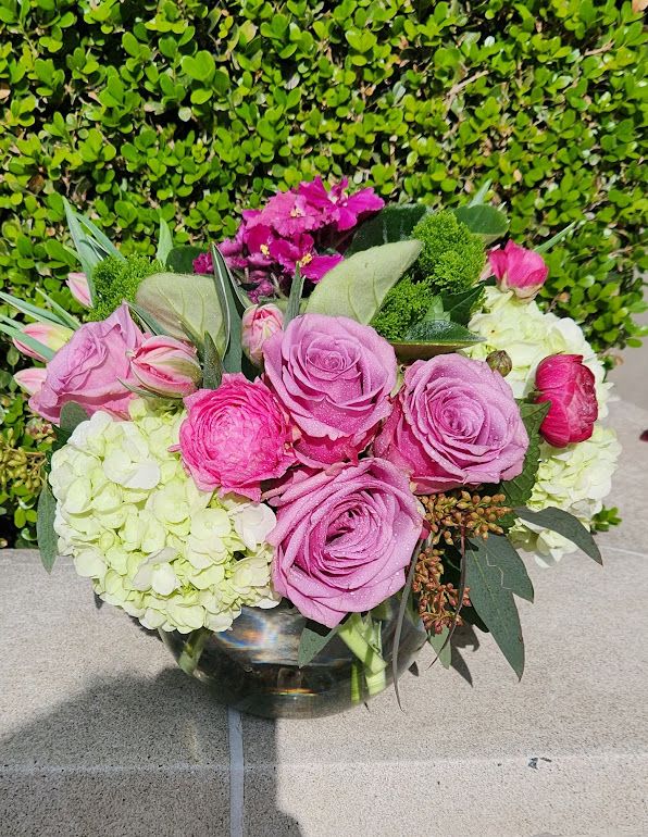 Low glass vase with pink roses, ranunculus, and green hydrangeas in a compact round bouquet
