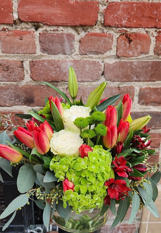 Mixed arrangement of red tulips, white roses, green hydrangeas and lilies in a clear glass vase