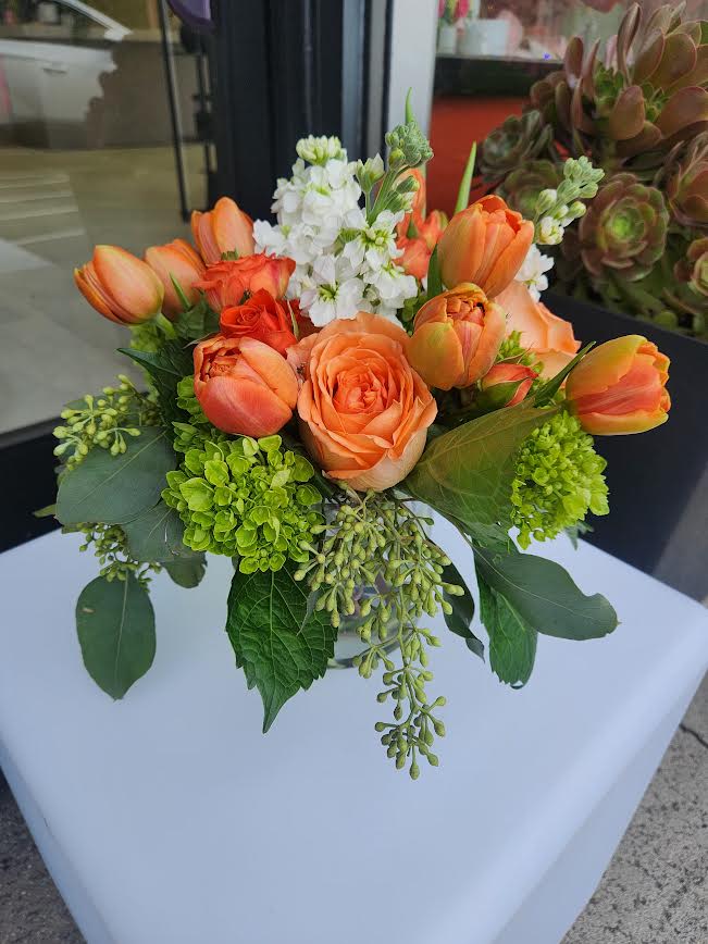 Compact orange rose and tulip arrangement with white blooms in a clear glass vase