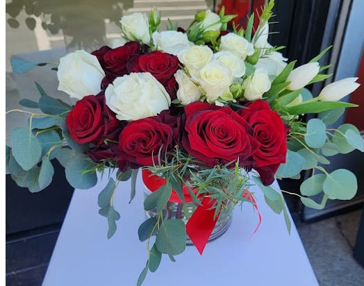 Low glass vase of red and white roses with white tulips and a red ribbon bow
