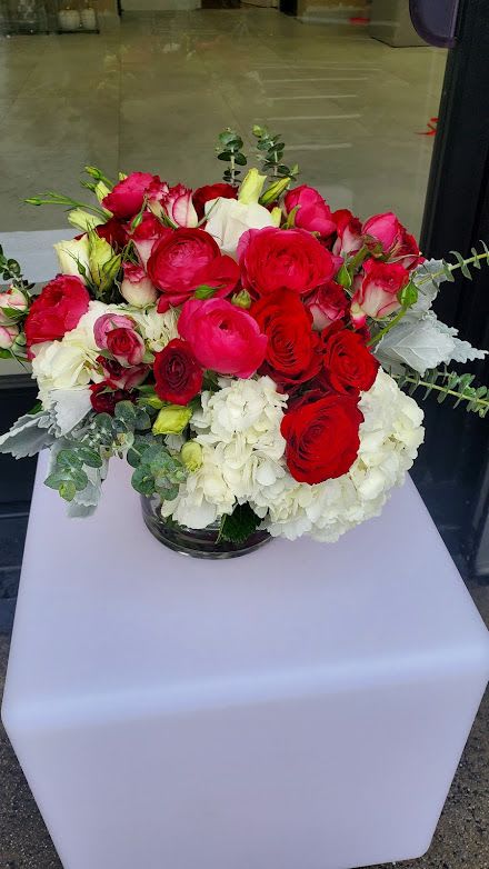 Low glass vase of red and hot pink roses with white hydrangeas on a white pedestal