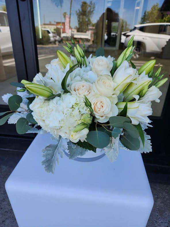 Low arrangement of white lilies, cream roses, and hydrangea in a round white vase