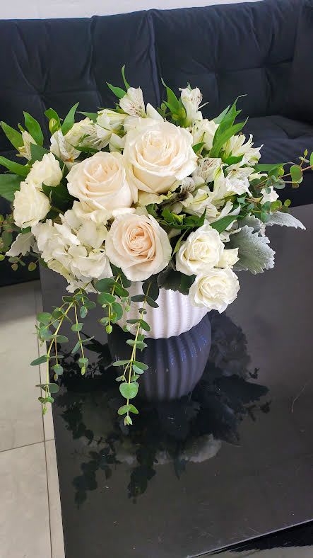 White and cream rose arrangement with greenery in a white textured pot on a black table
