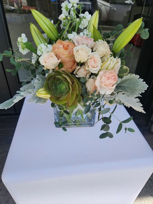 Peach and cream roses with lilies, white blooms, and a succulent in a clear square vase