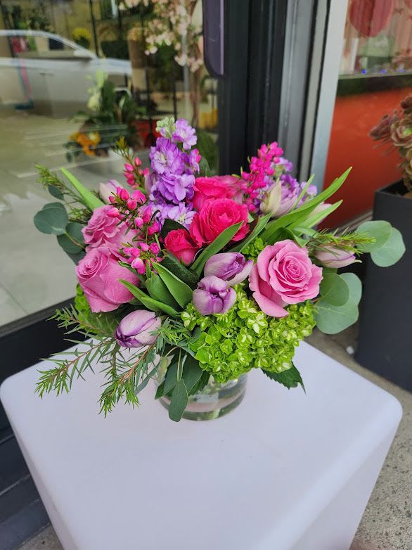 Low pink and purple flower arrangement with green hydrangea in a clear glass vase on a white table