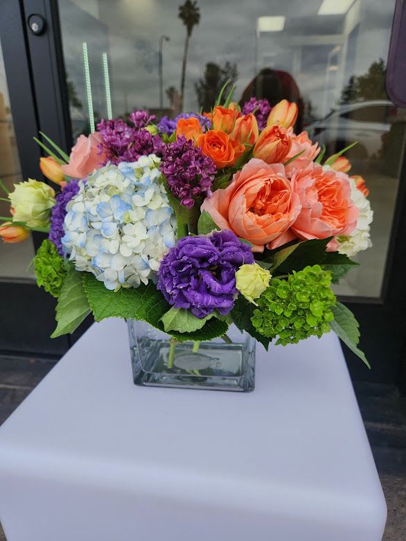 Low arrangement of bright mixed flowers in a clear glass cube vase