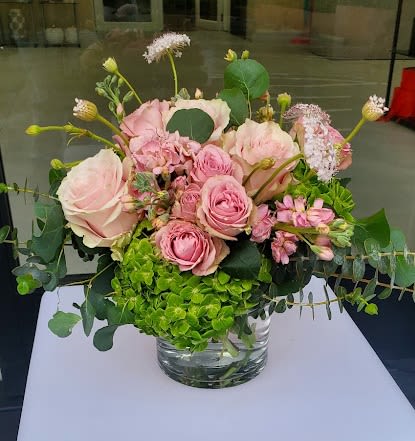 Low arrangement of pink roses and spray roses with bright green hydrangea in a clear glass vase