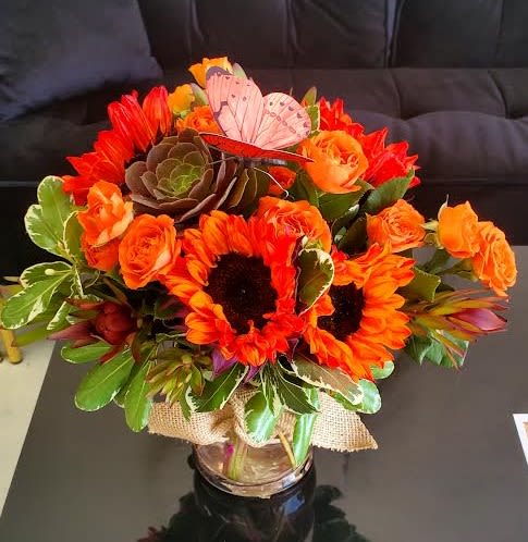 Bright orange sunflower and rose arrangement with succulent in a glass vase