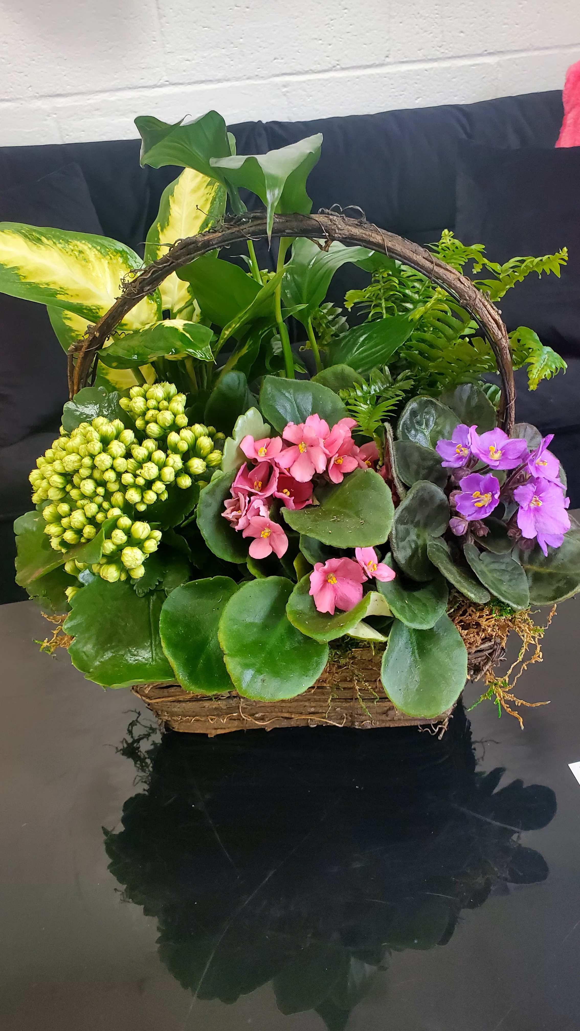 Basket garden of lush green plants with pink and purple flowering plants in a rustic handled basket.