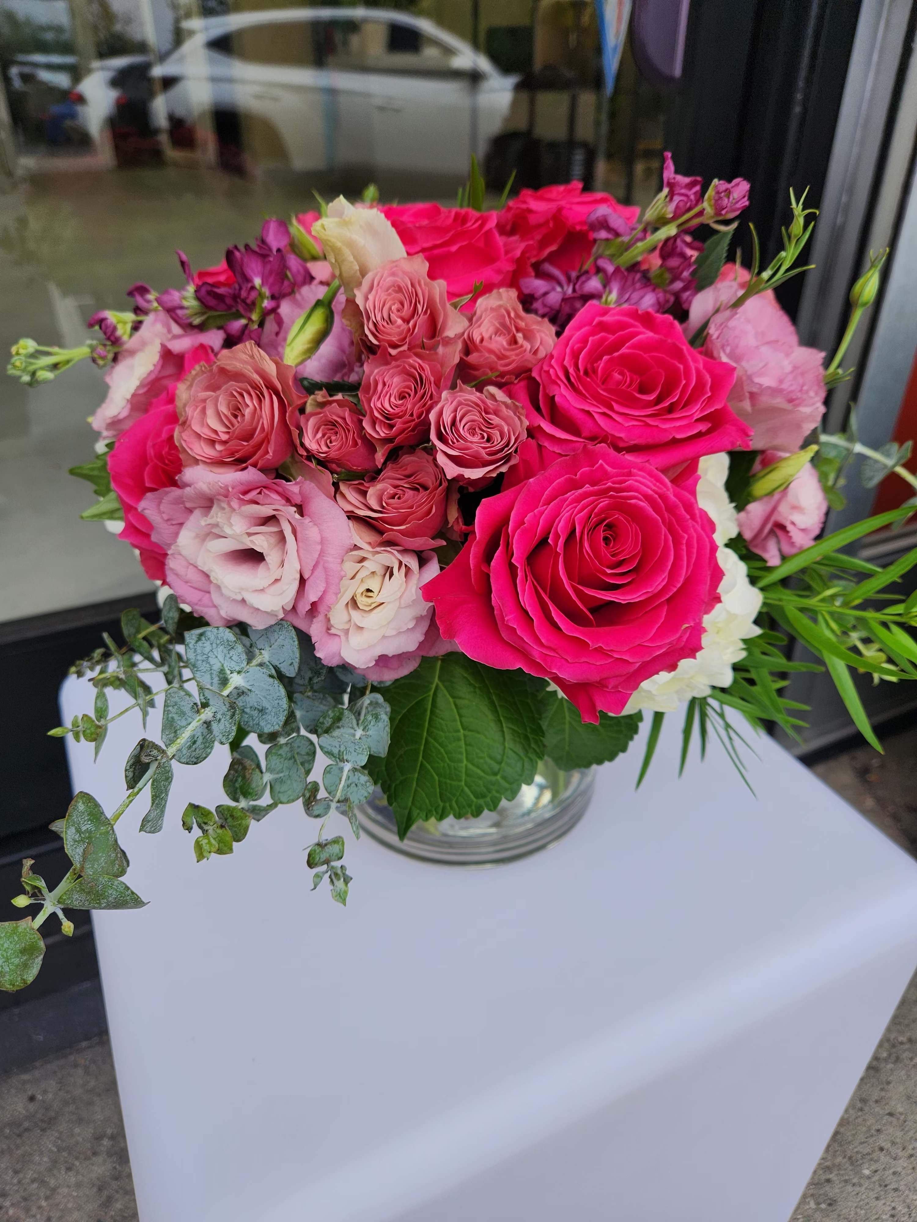 Low round arrangement of bright pink and blush flowers in a clear glass vase